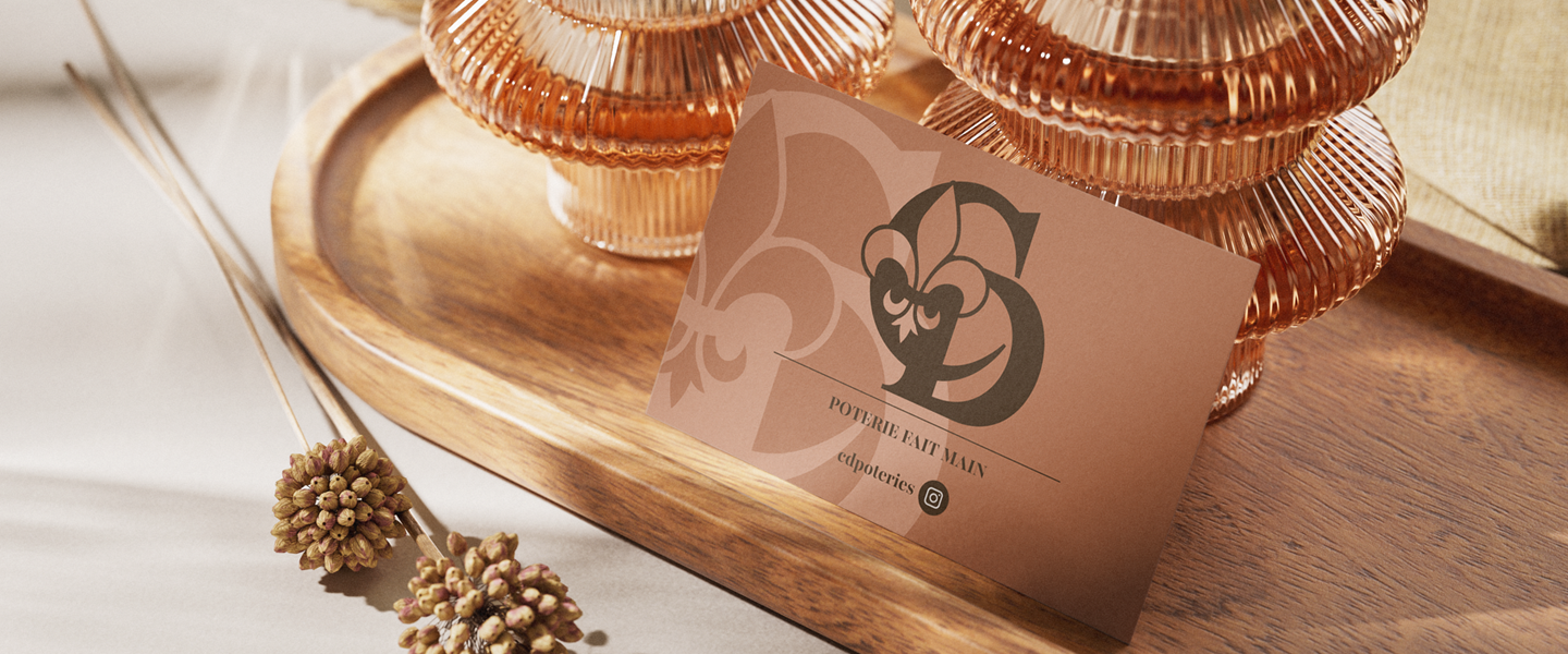 Carte de visite couleur brun-rosé de CD Poteries avec un logo monogramme fleur de lys foncé. Le design présente les initiales et le texte 'Poterie Fait Main' pour la créatrice de grès de Bréhan (Morbihan).